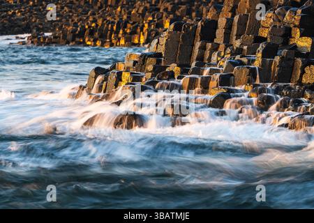 Am späten Nachmittag Sonnenlicht bei Nahaufnahme der Basaltsäulen des Grand Causeway, mit Wellen, die von ihnen abfließen. Giant's Causeway, Antrim Coast, Nordirland Stockfoto