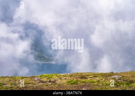 Ein atemberaubender und ruhiger Blick auf nebelbedeckte Berge, mit leuchtenden grünen Flecken und weichen, flauschigen Wolken, die sanft über eine ruhige und Idylle Rollen Stockfoto