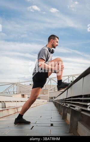Engagierter männlicher Athlet dehnt seine Beinmuskeln aus, um die Flexibilität zu erhöhen und Verletzungen vor einem rigorosen Training vorzubeugen Stockfoto