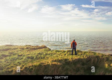 Alleinwanderer stehen auf einer sonnigen irischen Klippe und genießen das offene Meer – Freiheit, Abenteuer, Achtsamkeit und Küstenentfliehen. Stockfoto