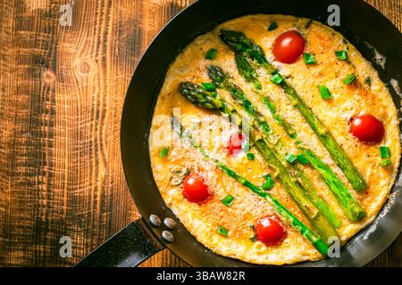 Spargel mit Rührei und Kirschtomaten in einer Pfanne auf hölzernem Hintergrund. Blick von oben. Leerzeichen für Text. Hochwertige Fotos Stockfoto