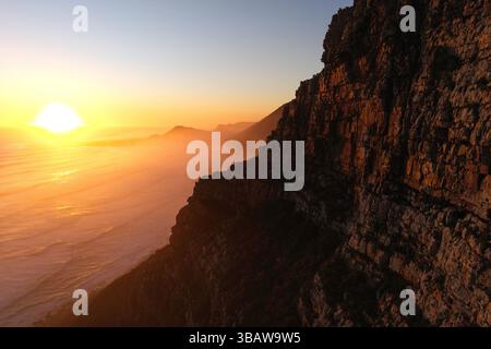 Misty Cliffs in Kapstadt, Südafrika am 13. Mai 2025 untergeht die Sonne über dem Atlantik in Misty Cliffs, Kapstadt, Südafrika. Misty Cliffs ist ein kleines Küstendorf im Cape Peninsulas Table Mountain National Park, etwa eine Autostunde südlich von Kapstadt. Bekannt für seine dramatische Landschaft und den häufigen Nebel des Ozeans liegt die Gegend zwischen Scarborough und Kommetjie, entlang der malerischen M65 Küstenstraße. Es ist Teil eines Naturschutzgebietes mit strengen Entwicklungsvorschriften, um seine unberührte natürliche Umwelt zu erhalten. Das Dorf wird von steilen Klippen und dem wi flankiert Stockfoto