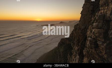 Misty Cliffs in Kapstadt, Südafrika am 13. Mai 2025 untergeht die Sonne über dem Atlantik in Misty Cliffs, Kapstadt, Südafrika. Misty Cliffs ist ein kleines Küstendorf im Cape Peninsulas Table Mountain National Park, etwa eine Autostunde südlich von Kapstadt. Bekannt für seine dramatische Landschaft und den häufigen Nebel des Ozeans liegt die Gegend zwischen Scarborough und Kommetjie, entlang der malerischen M65 Küstenstraße. Es ist Teil eines Naturschutzgebietes mit strengen Entwicklungsvorschriften, um seine unberührte natürliche Umwelt zu erhalten. Das Dorf wird von steilen Klippen und dem wi flankiert Stockfoto
