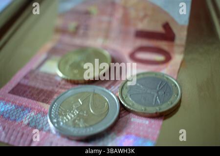 Drei Münzen und eine Banknote auf einem goldenen Tablett Stockfoto