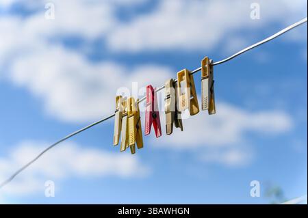 Bunte Plastiktüten hängen an einem Draht vor einem hellblauen Himmel mit weißen Wolken. Diagonale Komposition, Outdoor-Szene, starkes Sonnenlicht und s Stockfoto