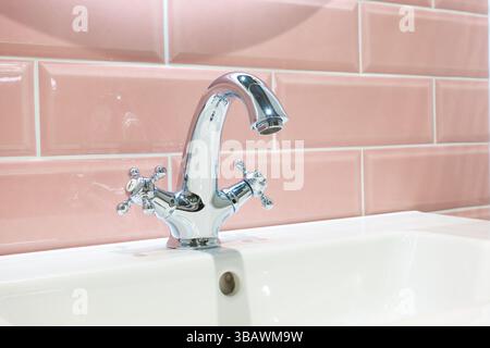 Farbenfrohes rosafarbenes Badezimmerkonzept mit rosafarbenen Fliesen und einem Chromarmatur im antiken Stil auf einem weißen Waschbecken Stockfoto