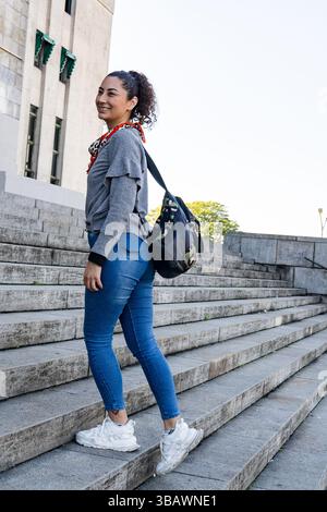 Eine junge Frau mit Rucksack klettert in einer städtischen Umgebung eine Steintreppe hinauf und schlägt vor, zu pendeln oder zu reisen Stockfoto