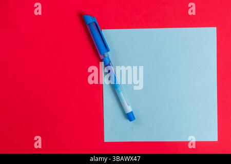 Eine Draufsicht eines blauen Stifts auf einem hellblauen Blatt Papier vor einem hellroten Hintergrund. Stockfoto