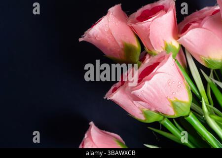 Rosafarbene künstliche Rosen mit weichen Wassertropfen auf dunklem Hintergrund. Perfekt für Schönheit, Romantik und dekoratives Design. Stockfoto