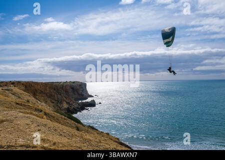 27.02.2025, Portugal, Algarve, Sagres - Gleitschirmfliegen am Stadtstrand Praia da Mareta, mit dem Aussichtspunkt Ponta da Atalaia hinten links. 00X Stockfoto