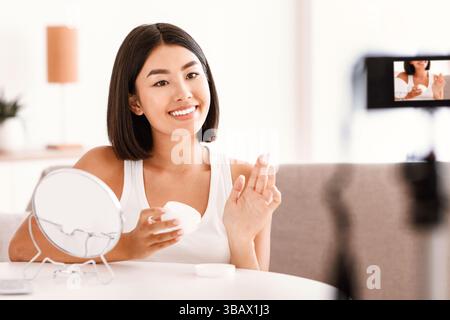 Junge Frau, die Creme auf ihr Gesicht für ihren Vlog Stockfoto