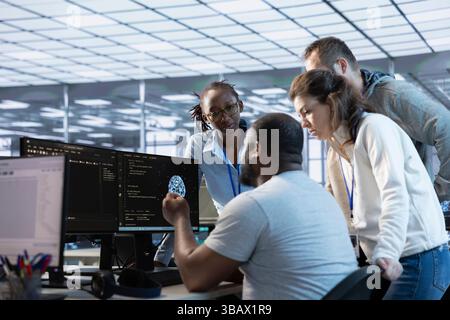 Team von Ingenieuren, die in der Serverfarm arbeiten und Daten mithilfe von PCs analysieren. Multiethnische Gruppe von Mitarbeitern, die die Infrastruktur im Rechenzentrum untersuchen und die Systemintegrität und -Sicherheit gewährleisten Stockfoto
