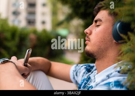 Ein junger Mann mit geschlossenen Augen, der draußen Musik hört. Stockfoto