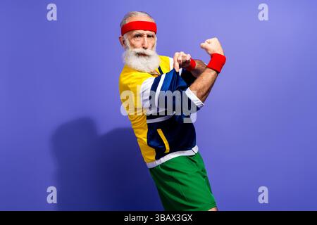 Ein selbstbewusster Senior-Mann in Retro-inspirierter Activewear mit Begeisterung vor einem leuchtend violetten Hintergrund Stockfoto
