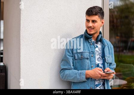Ein junger glücklicher, eleganter Mann, der ein Handy in der Stadtstraße benutzt. Stockfoto