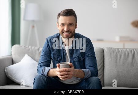 Entspannter schöner Mann, der Kaffee im Wohnzimmer trinkt Stockfoto