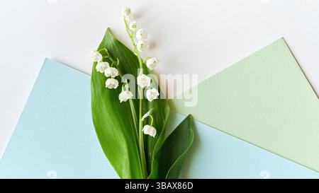 Nahaufnahme der zarten Maiglöckchen mit leuchtenden grünen Blättern auf pastellblauem und grünem geometrischem Hintergrund, die ein frisches und Stockfoto