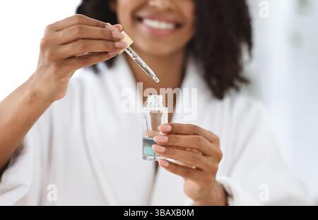 Schönheit Und Hautpflege. Lächelnde Schwarze Frau Holding Flasche Mit Feuchtigkeitsspendende Gesicht Serum Stockfoto