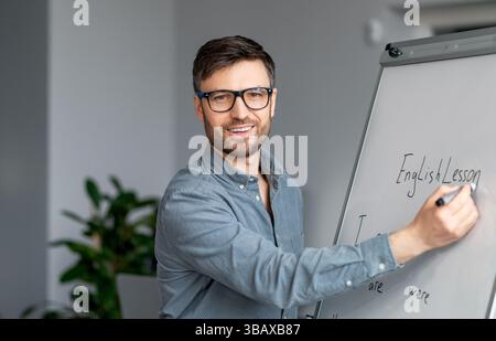Selbstbewusster reifer männlicher Lehrer, der Online-Unterricht gibt, neues Material erklärt, englische Regeln auf Tafel schreibt Stockfoto