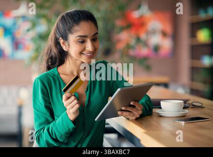 Fröhliche indische Dame Online-Banking, mit digitalen Tablet im Café Stockfoto