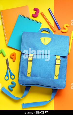 Stylischer Schulrucksack mit verschiedenen Schreibwaren auf farbigem Hintergrund Stockfoto