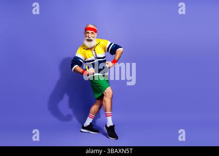 Energiegeladener Seniorenmann in Retro-Sportbekleidung, der eine lustige Pose auf einem lebendigen Hintergrund zeigt, zeigt lebendigen Geist und Vitalität Stockfoto