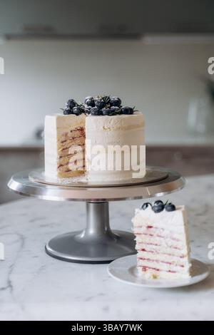 Ein wunderschön gestalteter Kuchen mit Blaubeeren auf einem Marmortisch. Ein Stück wird neben den Kuchen gelegt, um das köstliche Interieur hervorzuheben Stockfoto