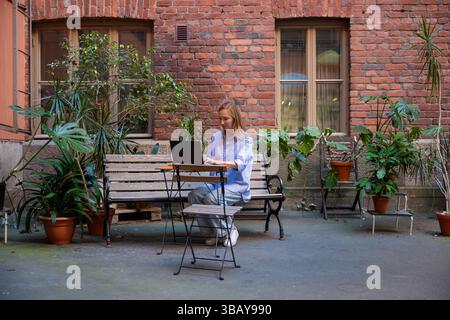 Frau arbeitet mit Laptop in einem gemütlichen Innenhof mit Topfpflanzen. Konzept der Fernarbeit oder Freiberufung Stockfoto