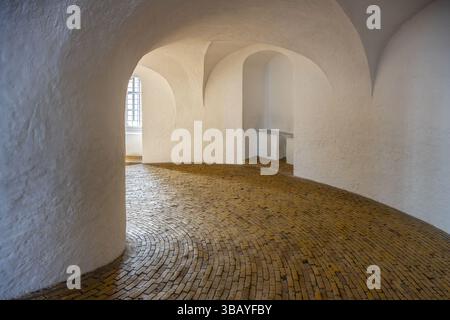 Besucher erkunden die gewundene Spiralrampe des Round Tower in Kopenhagen mit Holzfußboden. Dieses historische Gebäude bietet einzigartige architektonische Elemente und atemberaubende Ausblicke von oben. Stockfoto