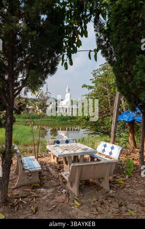 Von einem Garten-Schachbretttisch zu einem hohen weißen buddha, der auf einem kleinen Tempel neben einem Fluss in einem Weiler im Mae Yao-Unterbezirk in n sitzt Stockfoto