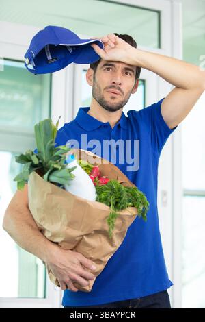Müder männlicher Kurier, der Lebensmittel bestellt Stockfoto