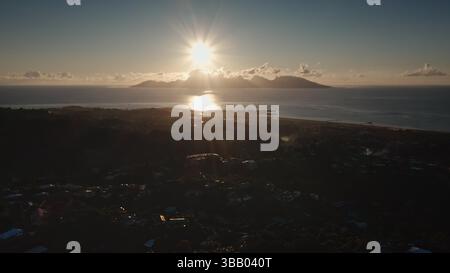 Aus der Vogelperspektive auf den Sonnenaufgang, der einen Starburst-Effekt über der Insel Moorea erzeugt, von Tahiti aus gesehen, wobei die Sonne auf dem Meer reflektiert und die Küste und die Stadtlandschaft beleuchtet Stockfoto