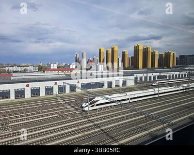 Hochgeschwindigkeitszug auf mehreren Bahngleisen in der Nähe von Hochhäusern in einer chinesischen Stadt an einem bewölkten Frühlingnachmittag. Stockfoto