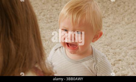 Mutter Sitzt Auf Dem Boden Der Lounge Und Tröstet Weinenden Baby-Sohn Stockfoto