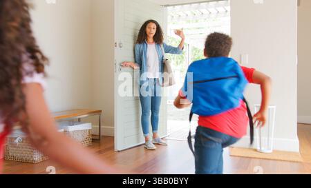 Mutter Steht Vor Der Haustür Und Ermutigt Die Kinder, Das Haus Zur Schule Zu Verlassen Stockfoto