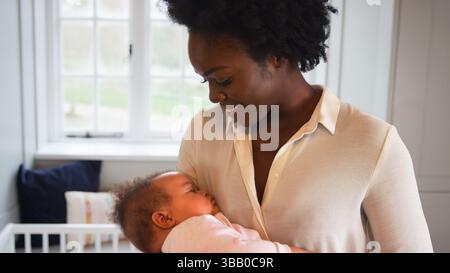 Nahaufnahme Von Lächelnder Neuer Mutter, Die Im Kinderzimmer Zu Hause Steht Und Schlafende Tochter Kuschelt Stockfoto