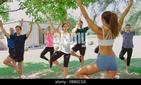 Weibliche Ausbilderin, Die Eine Gruppe Von Menschen Im Yoga-Kurs Im Freien Führt Stockfoto