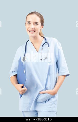 Junge Krankenschwester oder Ärztin lächelt, während sie ein Klemmbrett hält. Medizinisches Fachpersonal mit hellblauen Peelings und Stethoskop. Isoliert am Stockfoto