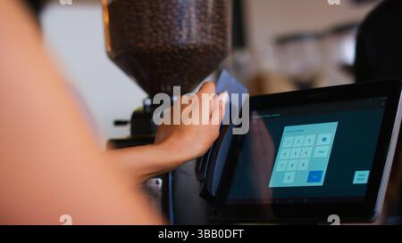 Nahaufnahme einer Mitarbeiterin im Café, die Personalausweis durch die Kasse zieht Stockfoto