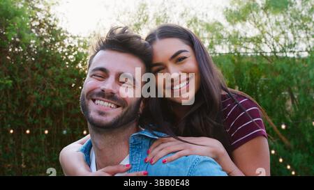 Portrait Von Paar Mit Mann Geben Frau Huckepack Zu Hause Im hinteren Garten Stockfoto