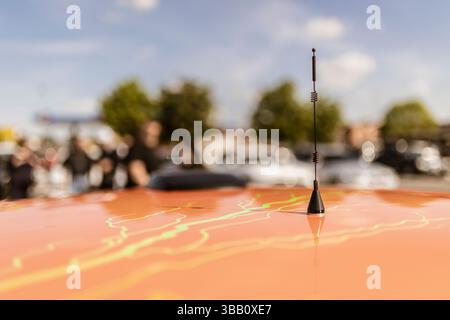 Nahaufnahme einer Radioantenne auf einem hell angepassten orangefarbenen Autodach mit einer unscharfen Menschenmenge im Hintergrund Stockfoto