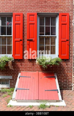 Philadelphia, USA – 20. Juli 2013: Ein rotes Fenster und eine abgewinkelte Kellertür an einem historischen Backsteinhaus in Philadelphia. Stockfoto