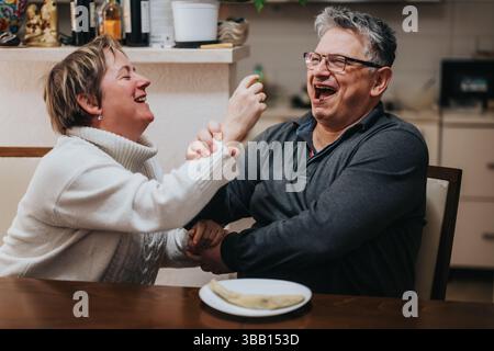 Glückliches Seniorenpaar lacht und genießt ein gemeinsames Essen zu Hause Stockfoto