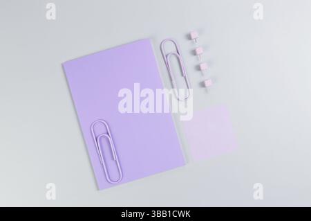 Draufsicht des lila Notizbuchs auf grauem Hintergrund. Violette Haftnotiz, Büroklammern und Stifte. Schule, Bürotapete. Flache Ladefläche, Kopierraum. Stockfoto
