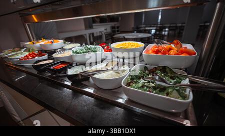 Farbenfrohes Selbstbedienungssalat-Buffet mit einer Auswahl an frischem Gemüse einschließlich Tomaten, Mais, Zwiebeln, Salat, Rucola, Kirschtomaten und Saucen, Stockfoto