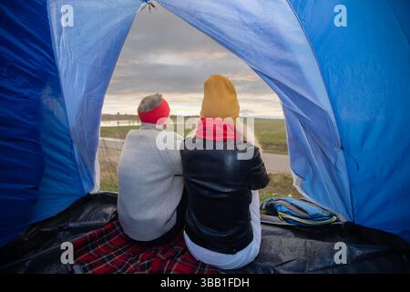 Aktives älteres kaukasisches Paar, das sich in einem Zelt vor dem Hintergrund der herbstlichen Naturlandschaft entspannt. Mann und Frau Touristen auf einer Reise. Stockfoto