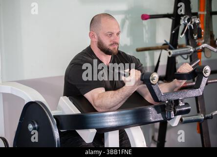 Ein Mann arbeitet an einer Maschine mit einem schwarzen Hemd. Er konzentriert sich auf sein Workout und ist in ernster Stimmung Stockfoto