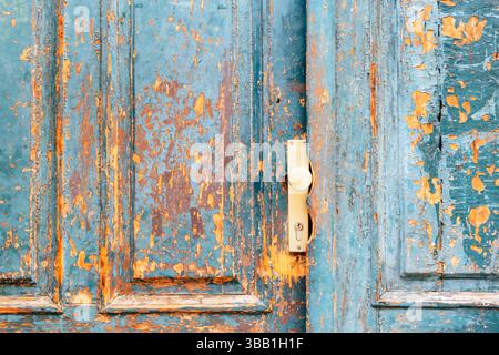 Alte Holztür mit abblätternder blauer Farbe und beigefarbenem Griff. Stockfoto