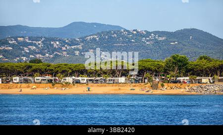 Malerische Aussicht vom Meer auf einen Sandstrand und einen Campingplatz mit Wohnmobilen, die unter dichten Baumdächern geparkt sind. Ruhiges blaues Meer im Vordergrund, Wald Stockfoto