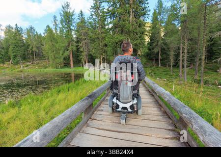Personen, die Rollstuhlfahrer sind, navigieren auf zugänglichen Wegen in den Dolomiten, umgeben von üppigem Grün in Italien. Die ruhige Landschaft bietet eine friedliche Atmosphäre Stockfoto